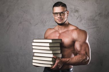 Bir yığın kitabı olan zeki ve kaslı bir adam. Vücut geliştirmede bilgi kavramı.