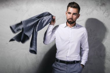 Gri takım elbiseli yakışıklı adam beton duvara karşı poz veriyor.