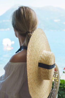 Geniş kenarlı şapkalı kadın dağlardaki göle bakıyor.