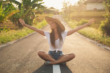 Genç mutlu kadın asfalt yolun ortasında oturuyor.