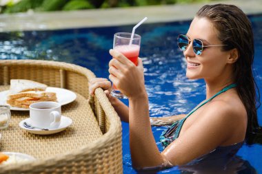 Tatil köyünde tatiller. Havuzda yüzen kahvaltısı olan mutlu genç bir kadın..