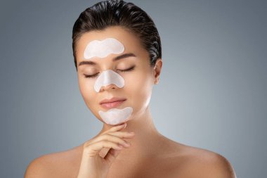 Yüzünde temizleyici gözenek şeritleri olan genç ve güzel bir kadın.