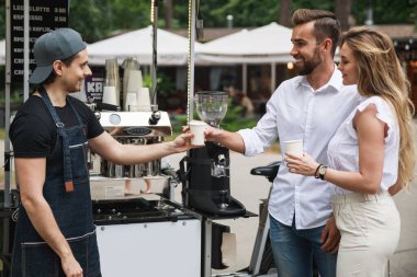 Barista denen adam caddedeki taşınabilir kahve dükkanında genç bir çifte kahve satıyor.