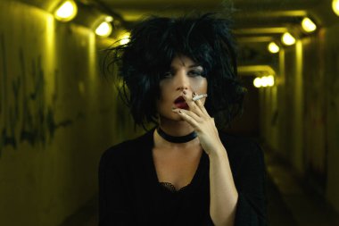 Karanlık yeraltında sigara içen siyah saçlı ucube kadın.