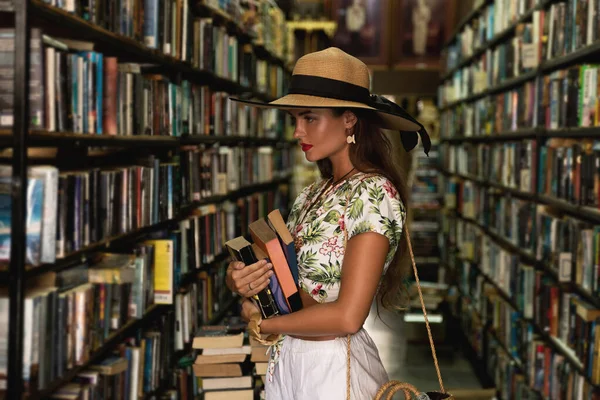 Beautiful girl wearing stylish outfit looking for interesting book in the small vintage bookstore