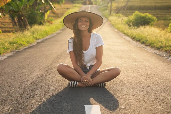 若い幸せな女性はアスファルトの道路の真ん中に座っている — ストック写真