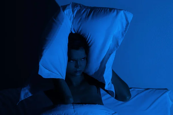 Woman in the bedroom with a pillow on her head because she don\'t wanna hear noise