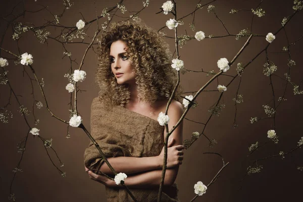 Portrait of lovely young woman with Afro hairstyle and beautiful make-up with a lot of white flowers on background