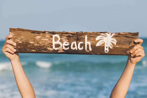 女性の手が文字で古い木の看板を保持 ビーチ — ストック写真