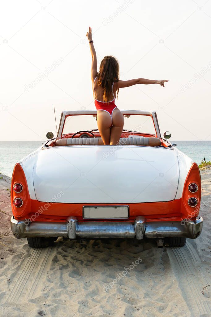 Sexy woman wearing  red swimsuit  is sitting inside a retro cabriolet car on the beach