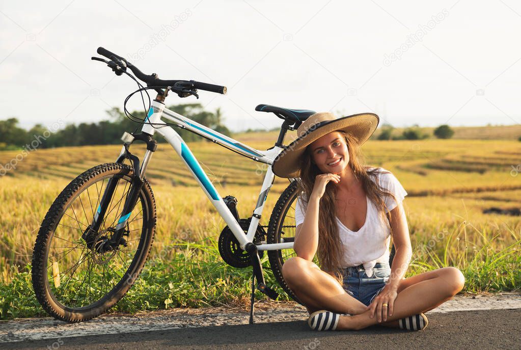 Young and happy woman with a bicycle on side of the road