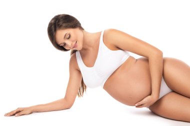 Genç ve güzel hamile kadın beyaz arka planda iç çamaşırı giyiyor.