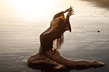 Siyah tunik giyen seksi ve ıslak kadın kumsalda siyah kumla poz veriyor.