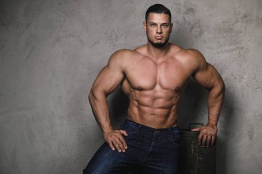 Beton duvarın yanında poz veren acımasız bir vücut geliştirici.