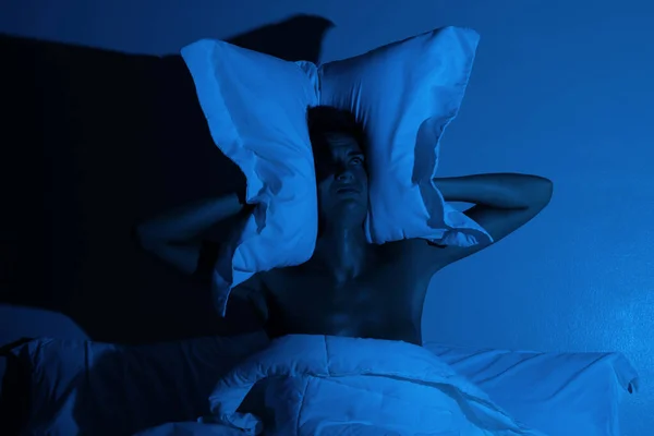 Woman in the bedroom with a pillow on her head because she don\'t wanna hear noise