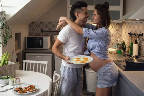 若く幸せな夫婦は赤ん坊を待っている 夫と妊娠中の妻は朝食時にキッチンで — ストック写真