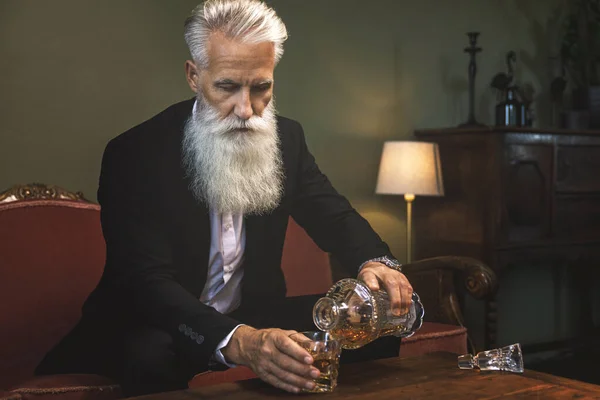 又时髦又英俊的大胡子老人往杯子里倒威士忌 — 图库照片