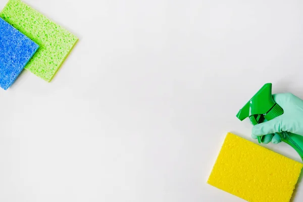 Detergents in spray. Cleaning accessories. Top view of green cleaning supplies on white background. Hand in green rubber glove. Close up.