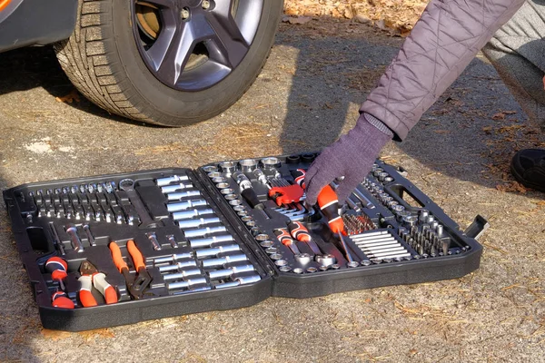Car driver using different repair tools for repairing a car. Tool set near the orange auto. Closeup picture of mechanic tools in box.