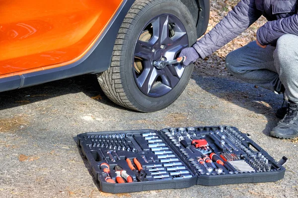 Car driver using different repair tools for repairing a car. Tool set in box near the orange auto. Automobile maintenance concept.