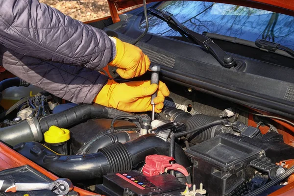 Car maintenance and repair concept. Hands of driver in orange rubber gloves checks car using tools, open hood. Automobile and transportation, close up.