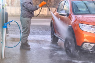 Adam turuncu arabasını dışarıda yıkıyor. Oto yıkamada su jeti ile temizlik, sabunlu su akıyor..