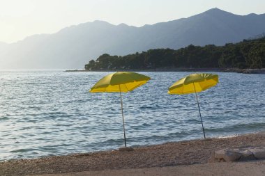 Rahatlamak için sarı şemsiyeler ve huzurlu deniz plajları. Mutlu yaz tatilleri ve turizm konsepti. Sunset 'teki deniz manzaralı plajlarda ücretli hizmet..