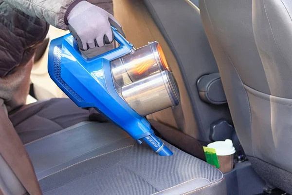 Vacuum cleaner in hands of driver. Cleaning of interior of the car with blue vacuum cleaner. Car textile seats is regular clean up.