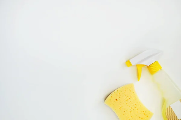 Cleaning agent in a spray bottle. Top view of cleaning product and yellow sponge on white background. Closeup. Copy space.