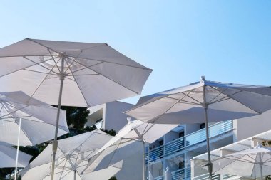 Deniz kıyısındaki otelin terasında dinlenmek ve rahatlamak için beyaz plaj şemsiyeleri, şemsiyeler ve şezlonglar. Mutlu yaz tatilleri ve tatil beldeleri.