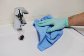 Férfi kéz gumi védő kesztyű kék mikroszálas rongy tisztítja vízvezeték a fürdőszobában. Házimunka. Takarítás vagy rendszeres takarítás.