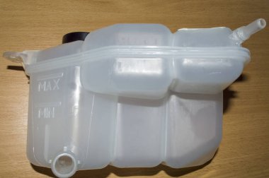Arabanın soğutma sisteminin beyaz plastik genişleme tankı ahşap bir masanın üzerinde duruyor.