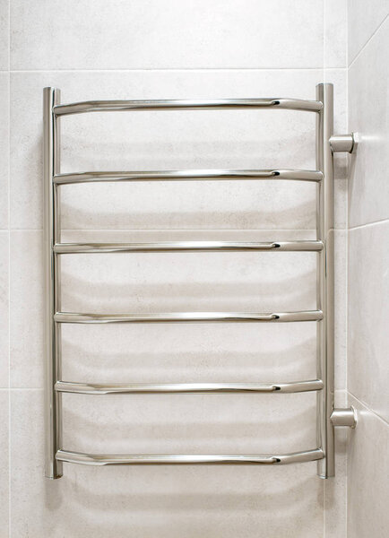 Modern chrome heated towel rail hanging on gray ceramic tiled in the bathroom