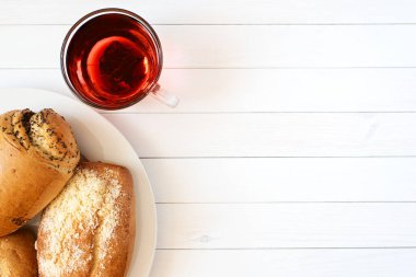 İçinde ev yapımı kekler olan cam bardakta amberçiçeği çayı. Beyaz ahşap bir masada kırmızı çay. Düz plan. Haşhaş tohumlu taze ev yapımı çörekler, kahvaltı