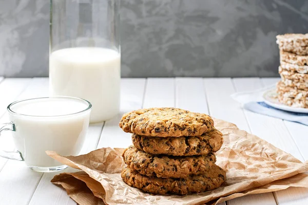 homemade oatmeal cookies with chocolate and milk. baking, milk in a decanter and a stack of cookies on a wooden table. healthy food