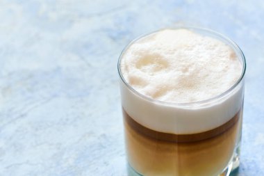 Mavi arka planda ev yapımı kahve makinesinde hazırlanmış cam bir fincanda kapuçino..