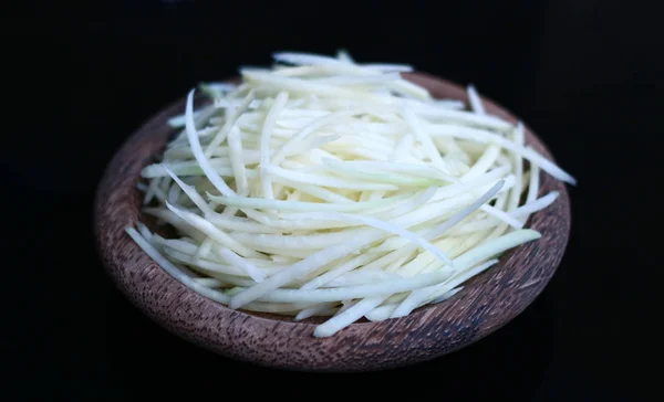 Shredded Green Papaya on wood plate with black background.