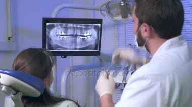 Diş hekimi hastanın x-ray fotoğrafını dişlerini tedavi sırasında gösterir.