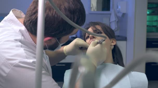 Дантист во время лечения сверлит зубы пациентке современной частной больницы — стоковое видео