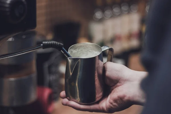 Hand with a pitcher. Whipping milk. Barista