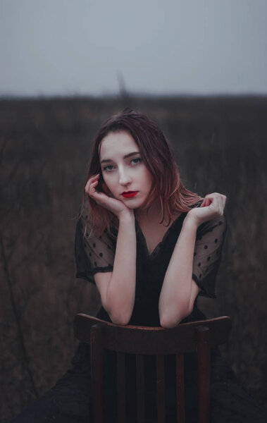 Beautiful girl with red lips sits on a chair in the field