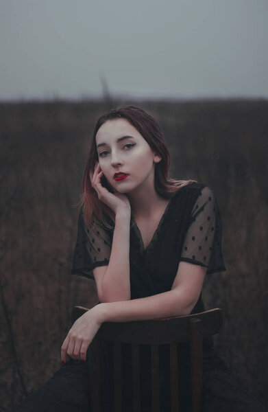 Beautiful girl with red lips sits on a chair in the field