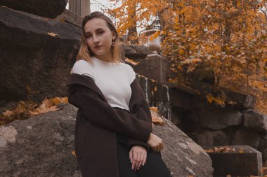 Paltolu genç kız ormanda bir taşın üzerinde oturuyor.