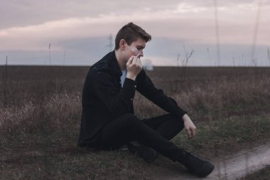 Confident guy smoking on the field. The guy in black. Thoughtful man