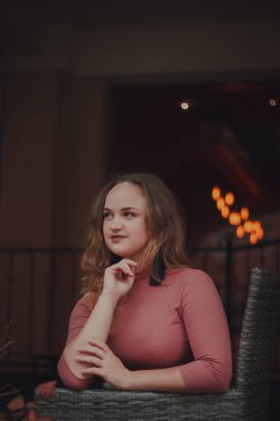 Terasta bir kafede güzel, zarif, mütevazı bir kız. Sıcak bir atmosfer. Hafif bir gülümseme ve arka planda bokeh 