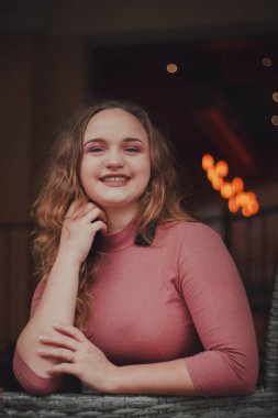 Terasta bir kafede güzel, zarif, mütevazı bir kız. Sıcak bir atmosfer. Hafif bir gülümseme ve arka planda bokeh 