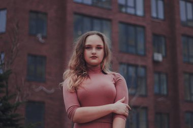 Kadın, şehirde akşam saatlerinde bir binanın önünde kollarını kavuşturarak güven içinde duruyor.