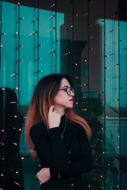 Gözlüklü, mavi cam arka planda kırmızı rujlu, kendine güveni tam bir iş kadını.