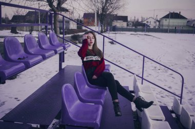 Mor tribünlerdeki kırmızı kazaklı kız. Moda portreleri. Üniversitenin yanındaki spor sahasında.