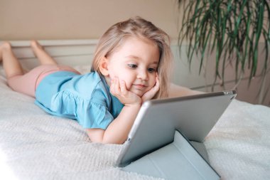 Güzel çocuk küçük kız evde yatakta yatarken tabletle oynuyor.. 